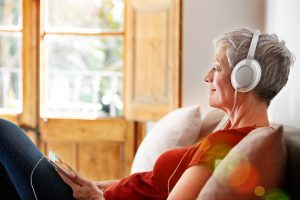 woman sits on couch with headphone. Listening to music is one of the ideas for social distancing.