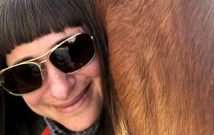 women with horse, smiling after seeing a gastroenterologist by way of a virtual visit to assure her she needed to go to the hospital.
