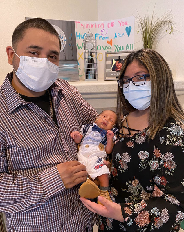 jade and Mikey, wearing masks and holding their newborn son.