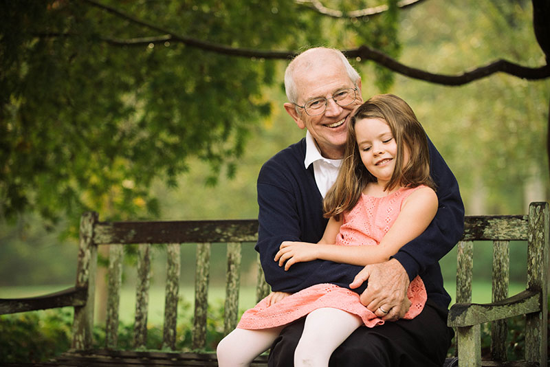 man, who is part of trial with blood pressure drug to fight pancreatic cancer, holding his granddaughter on a park bench.