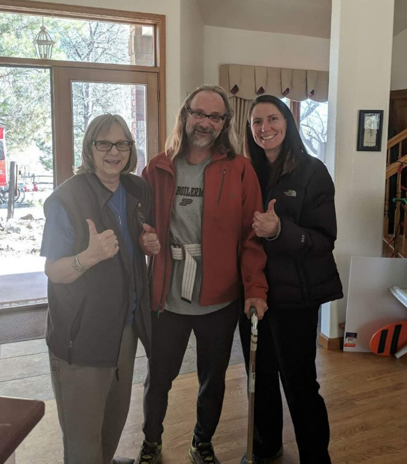 three people stand with their thumbs up inside Jeff's home as a sign that his home is safe to return to after Jeff's hemorrhagic stroke treatment