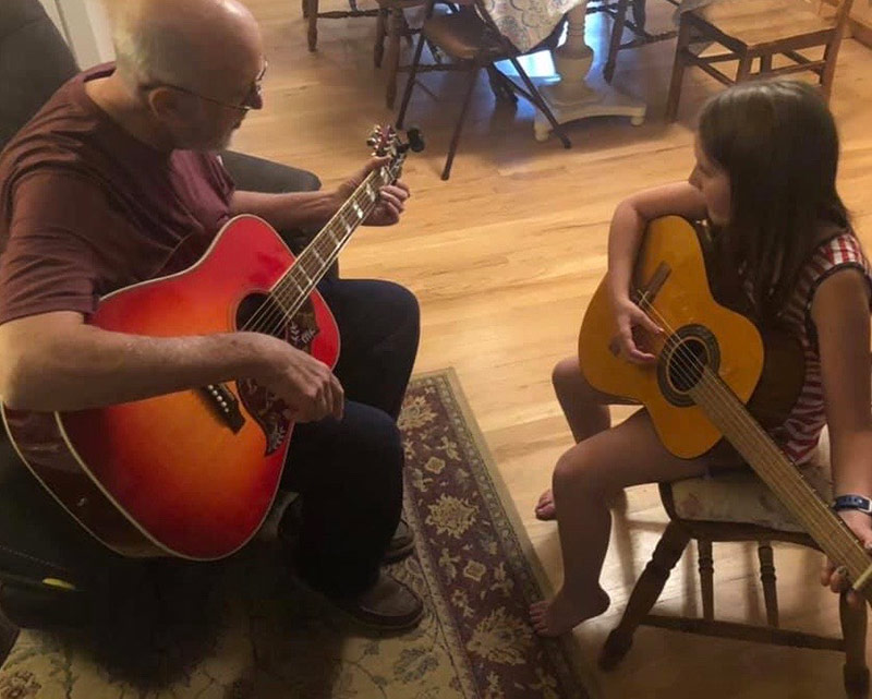Jim playing guitar with his granddaughter in the kitchen.