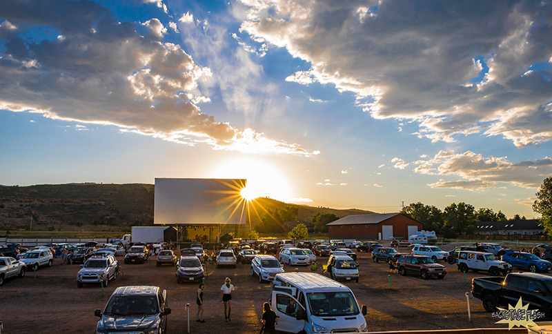 Drive-in theater in Fort Collins set up for live music concert, with sun setting behind the stage.
