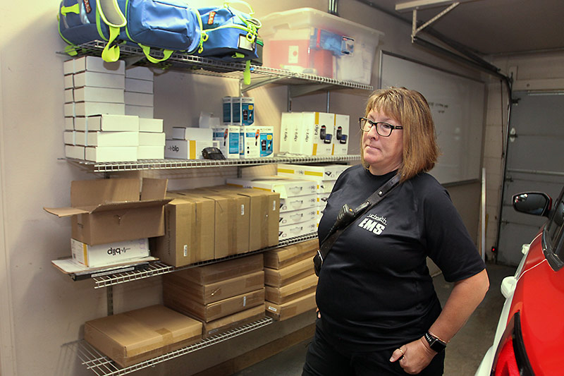 community paramedic stands in the garage with in-home monitoring supplies they use on the shelf.