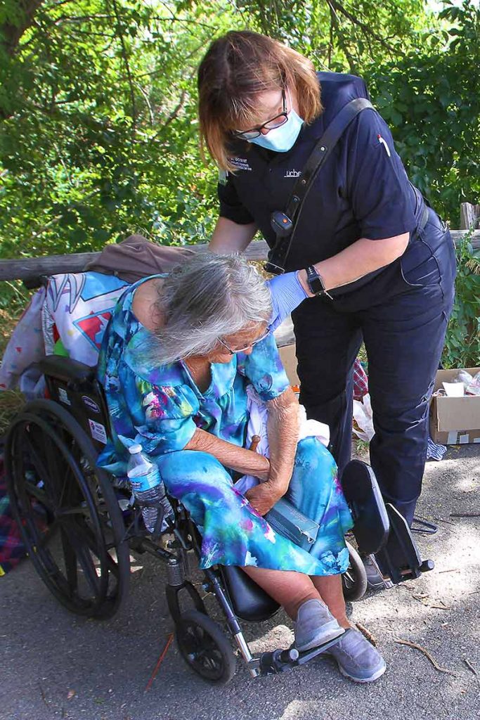 community paramedic feels the back of a homeless woman in a wheelchair at a park.