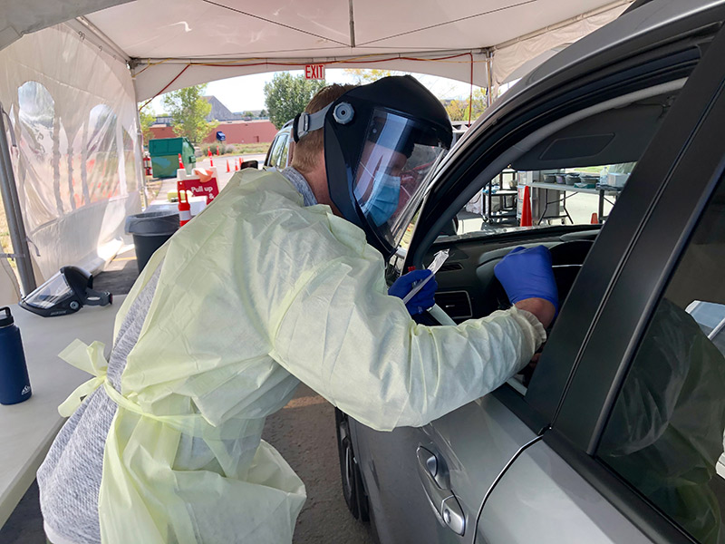 Testing is essential in the fight against COVID-19. Here a health worker in protective gear tests a person in a car at a UCHealth hospital.