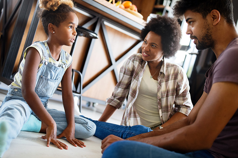 Parents need to consider a child's emotional health too when discussing emergency preparedness for kids as these parents are doing here talking to their child on the floor of their home.
