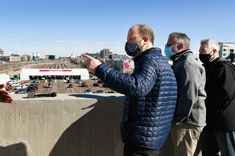 Gov. Polis peers from the fourth story of a parking garage down at a mass vaccination event on Saturday.