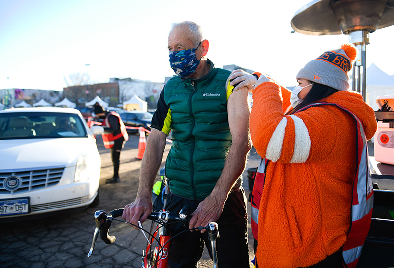 John Wethey, 72, rode his bike from Golden all the way to Coors Field in downtown Denver. Giving him his COVID-19 vaccine was Gabriela Marin.