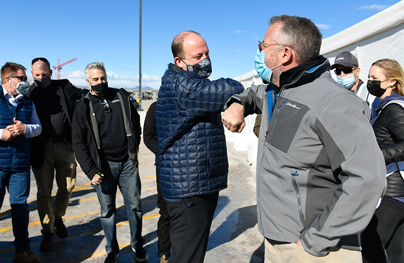 Gov. Jared Polis does an elbow bump with Dr. Richard Zane as he arrives at the mass vaccination event at Coors Field in Denver on Saturday. Manny Rodriguez of UCHealth stands to the governor's left.