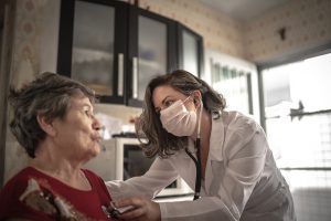 A doctor uses a stethoscope to hear any heart problems of an older woman who recovered from COVID..