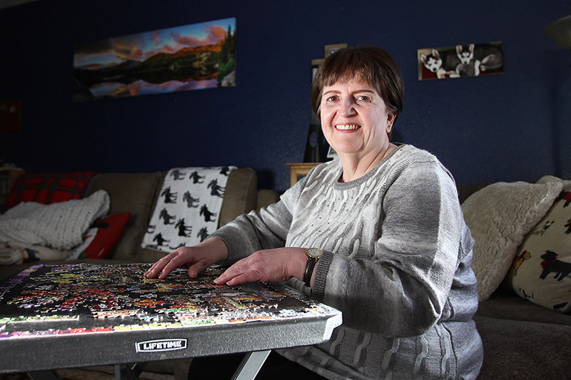 Deb HOffman doing a puzzle in her living room, one of the ways she is staying safe in her life after almost dying from COVID-19.