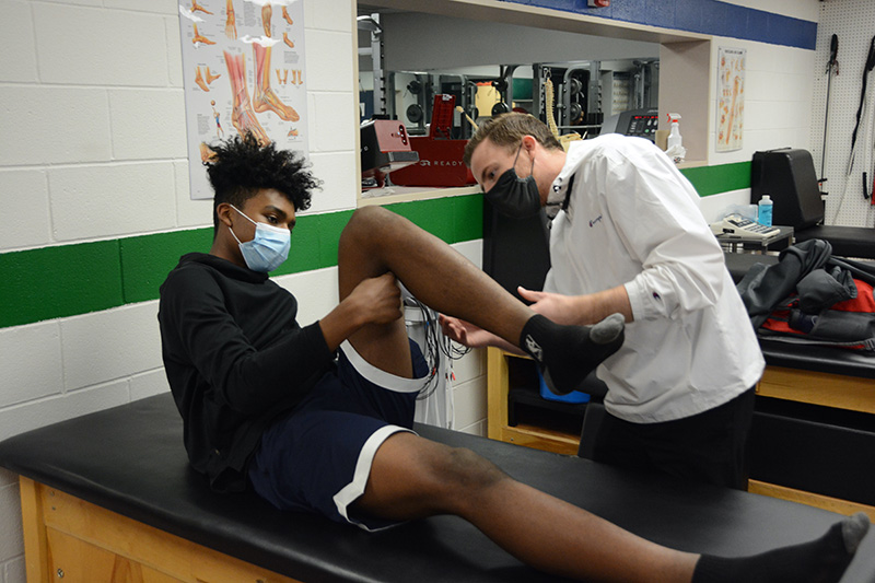 UCHealth athletic trainer, Kyle Thorson, works with student, Marzouq Abdur-Razaaq, after he hurt his knee during a basketball game.