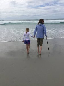 Amy walks on the beach with Sienna, aided by a cane. Lupus symptoms can make walking difficult.