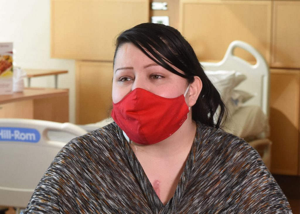 woman who had a heart transplant talks about the hospital wayfinding app feature while wearing a red mask.