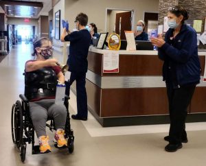 Care givers cheer for Barb Kotzian, who was born with dwarfism, as she rounds a corner at UCHealth Broomfield Hospital after rehab following her spine surgery.