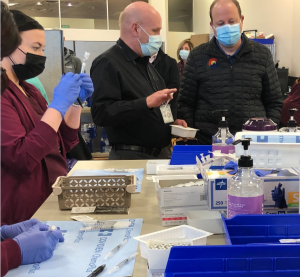 Larry Tremel, UCHealth's pharmacy director in southern Colorado, talks to Colorado Gov. Jared Polis as pharmacy techs prepare COVID-19 vaccinations.