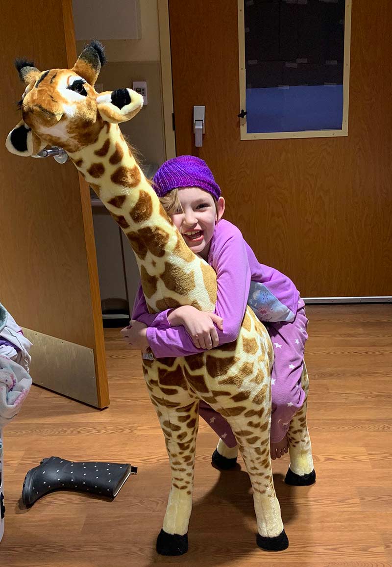 juno smith on a stuffed garaffe in the hospital, where her mom has become a blood donor.