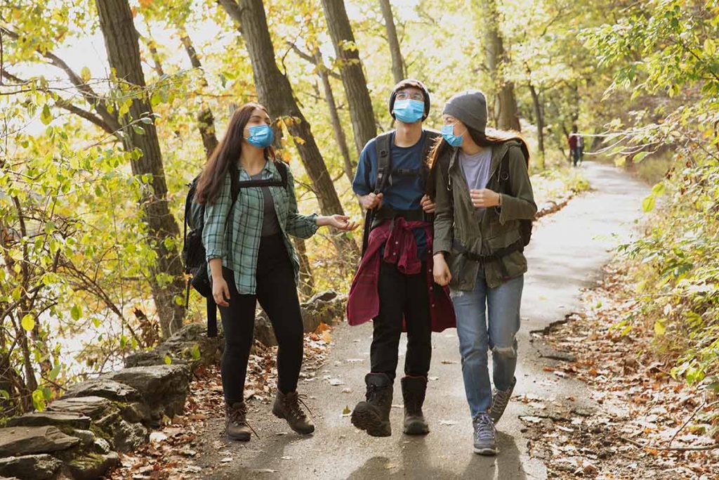 Three teens hike while wearing masks. CDC recently released new guidelines for wearing masks outdoors.
