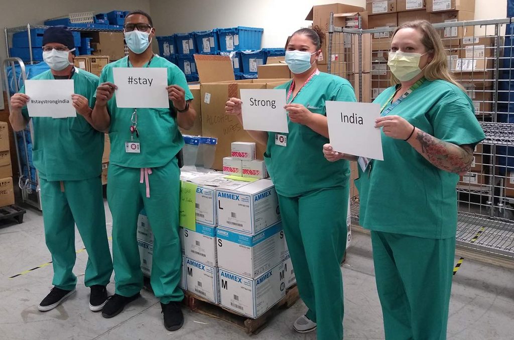 A photo of four health care workers holding up signs supporting the effort to send medical supplies to India.