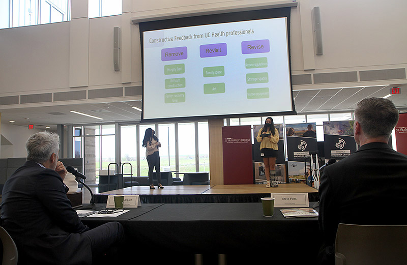 two girls from the Innovation Center of St. Vrain Valley Schools present on a large screen and stage.