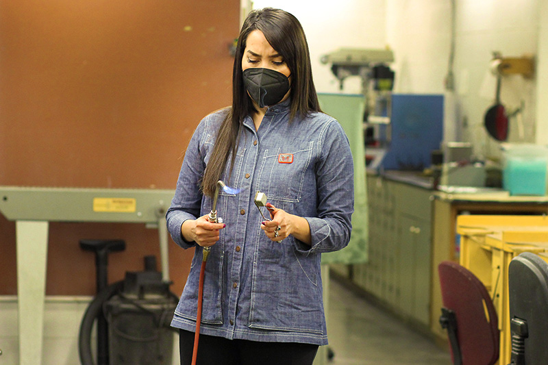 Priscilla Gonzalez holding a metalsmith torch. Her art demonstrates her efforts for colon cancer awareness.