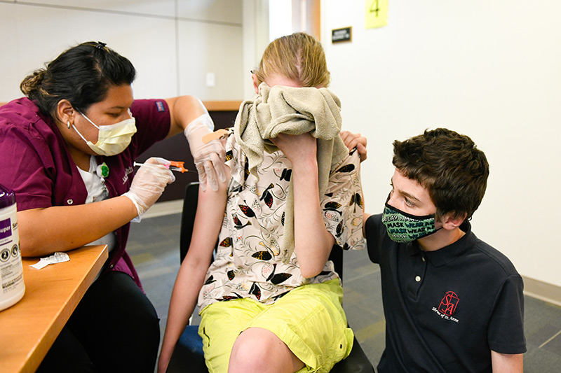 kids start getting their COVID-19 vaccines. Meghan Williams covers her face with the blankie she had when she was a baby as her brother, Wilson, 10, comforts her.