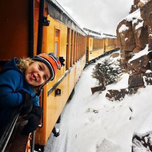 child holds his head out a train car on a scenic train ride in Colorado