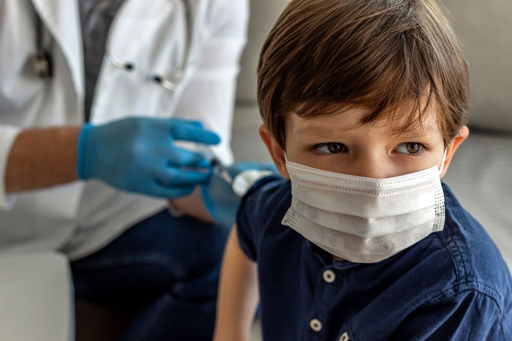 A boy wearing a mask receives a shot in his right arm.