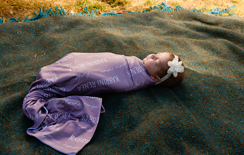 Kabrini Mays poses in a purple blanket with her name on it.
