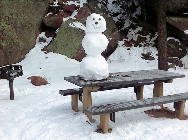 A snow man built on top of a picnic table.