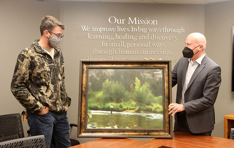 Kevin Unger, right, UCHealth President and CEO of UCHealth Poudre Valley Hospital and UCHealth Medical Center of the Rockies, gives a painting to 25-year-old Seth Kloberdanz. Also there presenting the painting to Seth was Ryan Rohman, chief operating officer for UCHealth Northern Colorado, and Grace Taylor, vice president of operations for UCHealth Northern Colorado. Photo by Kati Blocker, UCHealth.