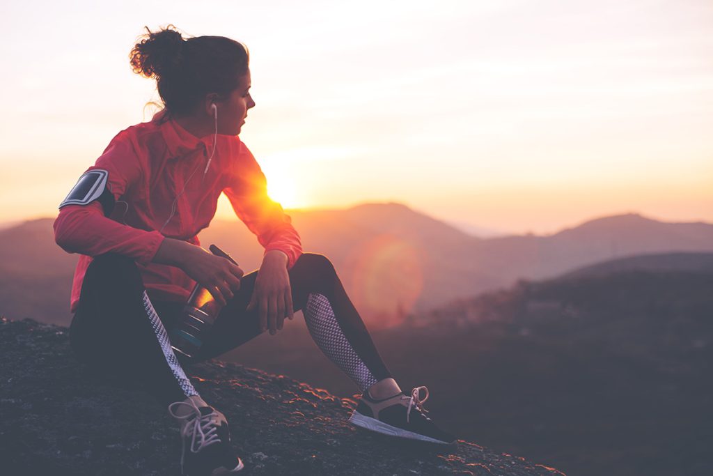 Woman relaxes atop a ridge and looks out over mountains. Timing of rest and recovery help prevent overtraining syndrome.