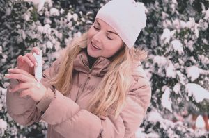A woman in a winter coat applying lotion to her hand, which has dry skin
