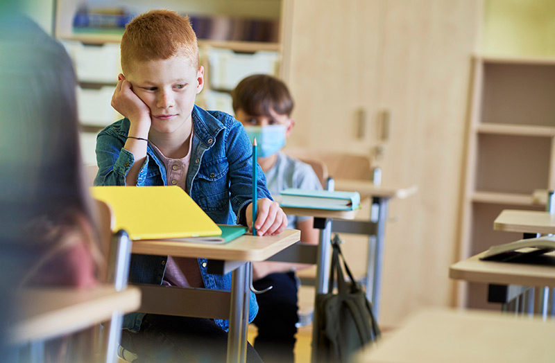 school child is wearing a mask while another isn't, which is what is happening as schools drop mask mandates.