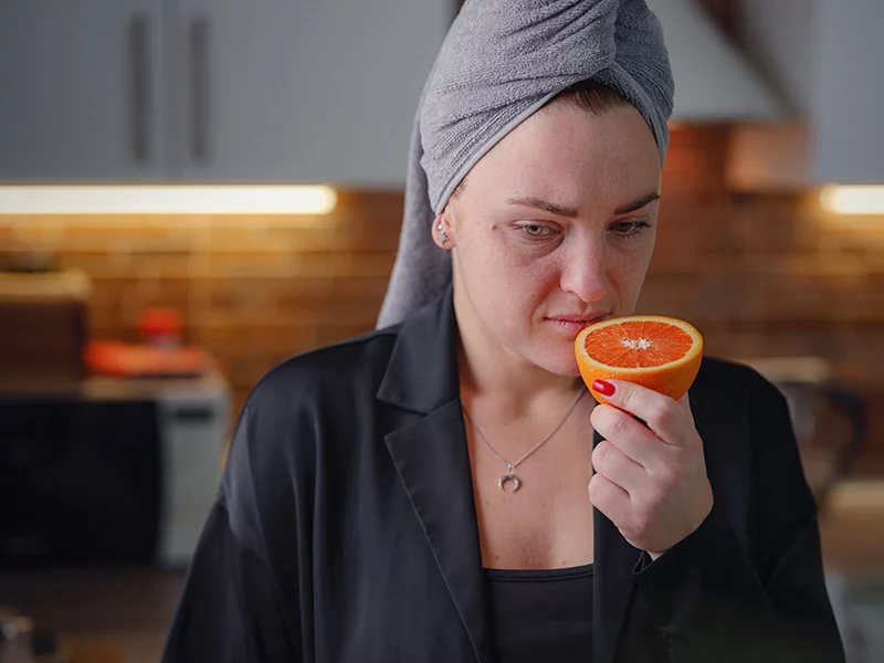 Sick woman smells an orange, trying to regain her sense of taste and smell after COVID-19.