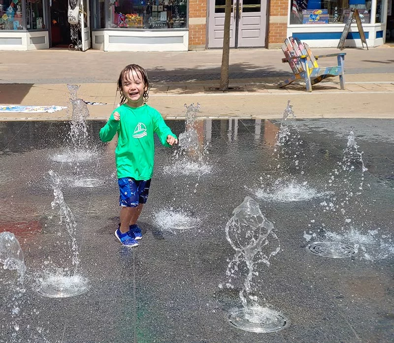 A young child enjoys the splash pad in Old Town Square. Photo by Kati Blocker, UCHealth.