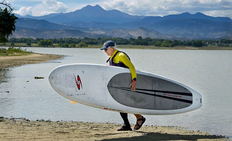 Bob Nicholson carries his standup paddleboard back to his van after an afternoon on McIntosh Lake in Longmont. It weighs more than 30 pounds. Photo by Sonya Doctorian, UCHealth