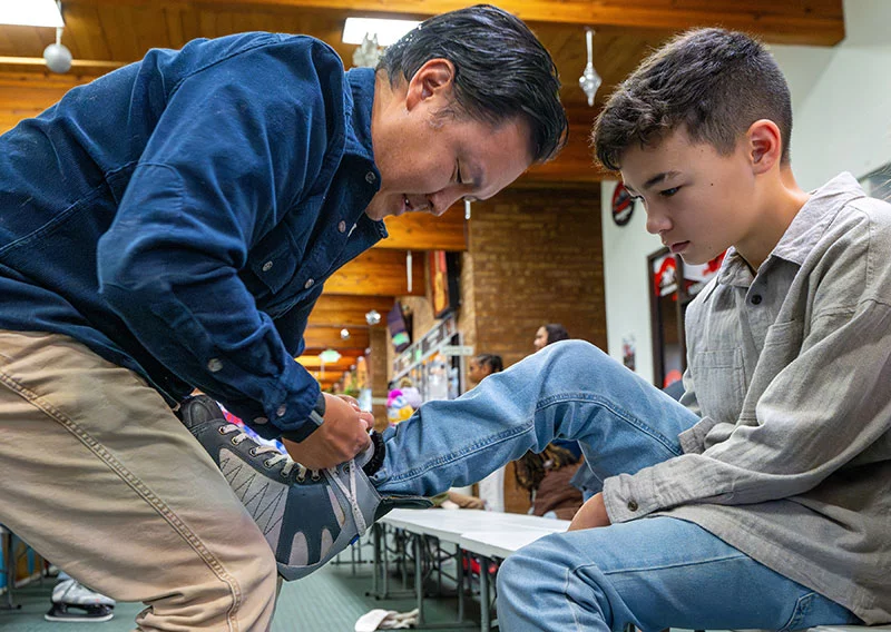 Lee helps his son, Cruz, lace up his ice skates at the Pueblo Ice Arena. The family also enjoys skiing - which Cruz said he prefers to skating. Photo by Mike Sweeney, for UCHealth.