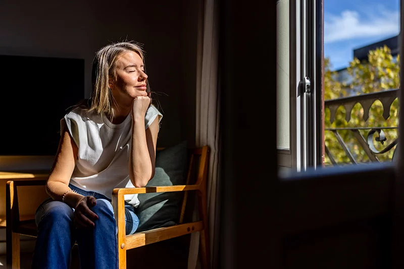 Woman sitting at a window with the sun shining on her face. Healthy stress management, lifestyle choices and intentional internal dialogue can play a key role in reducing emotional dysregulation. Photo: Getty Images.