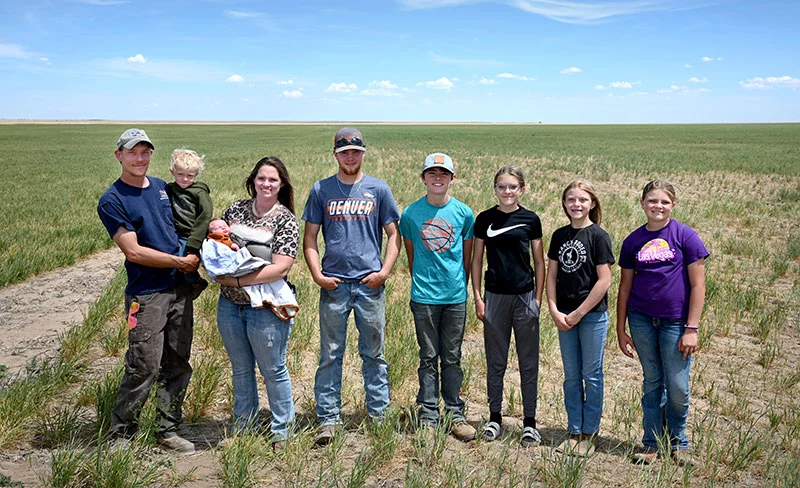 The family gathers in a neighbor’s field where Branden's oldest son, Kadan Dunlap, will spread fertilizer for his employer. From left to right, Branden holds Raeden Dunlap and Jade holds Beauden. Their children are: Kaden, 19, Landon Jacquart, 12, Hadlee Dunlap, 12, Kynlee Dunlap, 11, and Sadie Jacquart, 10. Photo by Sonya Doctorian.