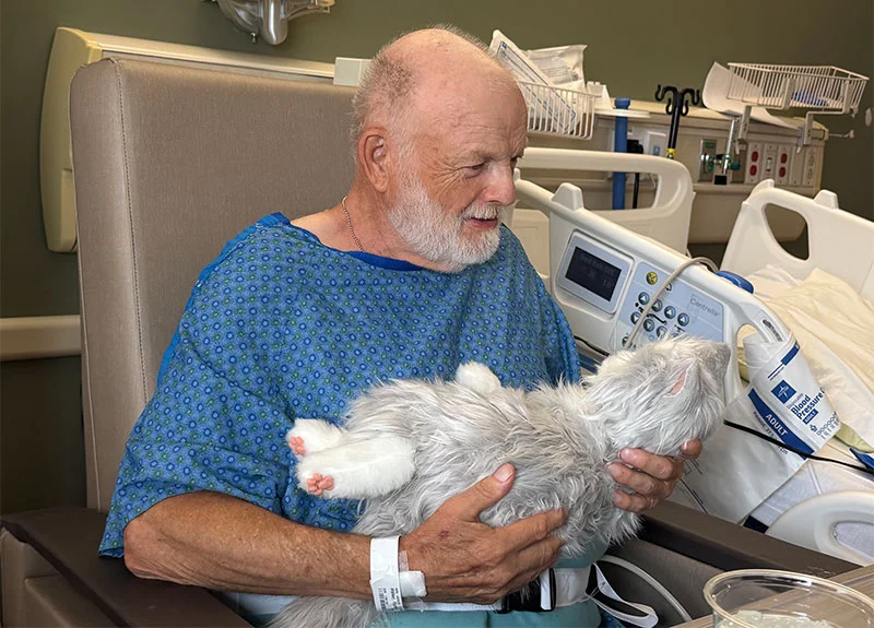 Robotic companion pets such as the cat Richard Walker holds are having a strikingly positive effect on elderly patients with dementia as well as care providers and families in UCHealth University of Colorado Hospital’s Acute Care for the Elderly unit. Photo courtesy of Donna Delano.