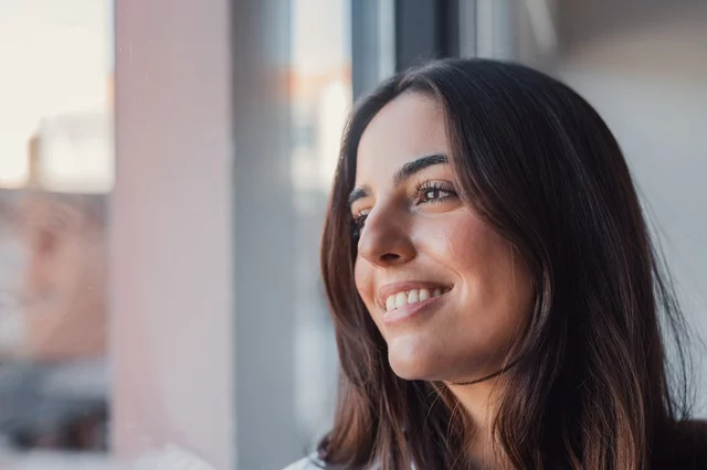 Mujer sentada junto a una ventana con el sol iluminándole el rostro. Una gestión saludable del estrés, las decisiones sobre el estilo de vida y un diálogo interno consciente pueden desempeñar un papel clave en el bienestar emocional. Foto: Getty Images.