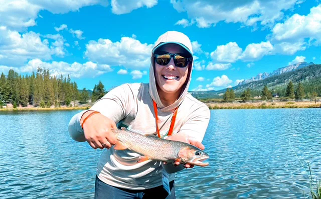 Karissa holding a fish at a lake. A Wyoming native and outdoor enthusiast, Karissa Goossen persevered through breast cancer, thyroid cancer and ongoing cancer surveillance after learning she carries a CHEK2 gene mutation. She posed for this photo during a flyfishing retreat with Casting for Recovery, a group that supports female cancer patients. Photo courtesy of Karissa Goossen.