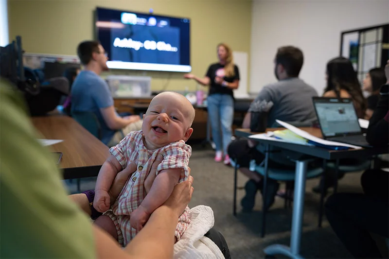 A baby grins during a group prenatal visit in the Denver area. Baby Noelle, then 7-weeks-old, grins happily in her mom, Erin Melzer's lap during a breastfeeding class at UCHealth Family Medicine in Westminster. Dr. Vivan Jiang and her team offer group prenatal visits rather than short one-on-one checkups because they help both moms and babies thrive. Photo by Mark Reis, for UCHealth.