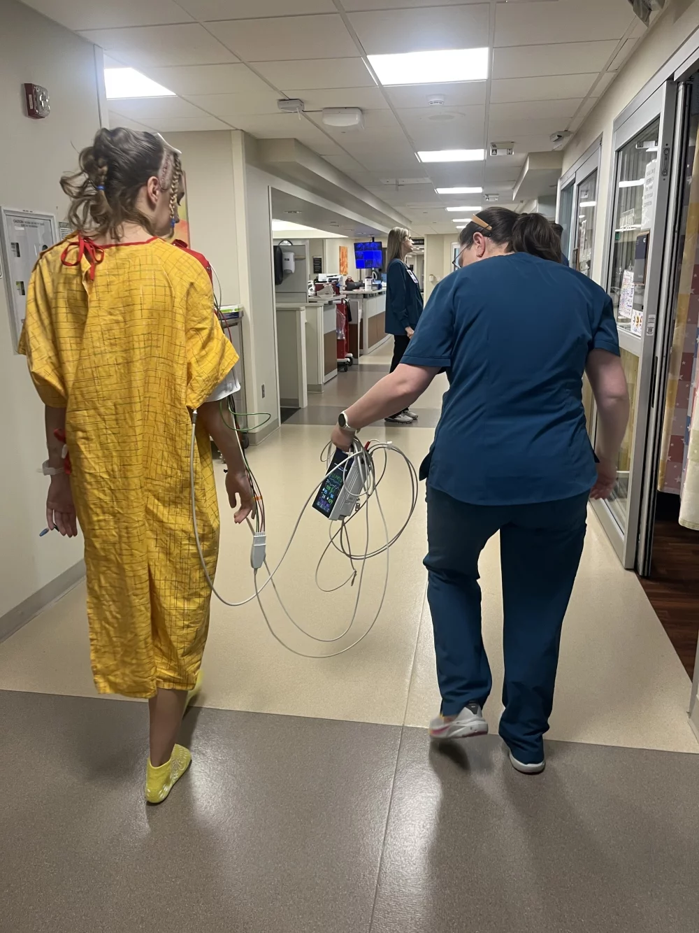 Kadyn walks down a hallway at a hospital unit with a rehabilitation staff member