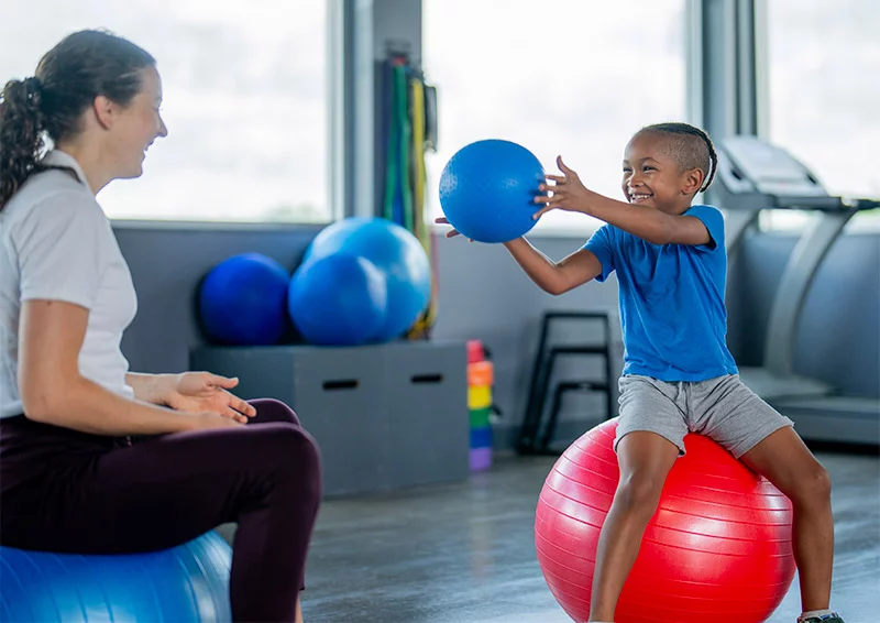 Child passing a ball to their occupational therapist. Along with skill building, occupational therapists can help a child develop gross and fine motor skills, vision skills and emotional regulation. Photo: Getty Images.