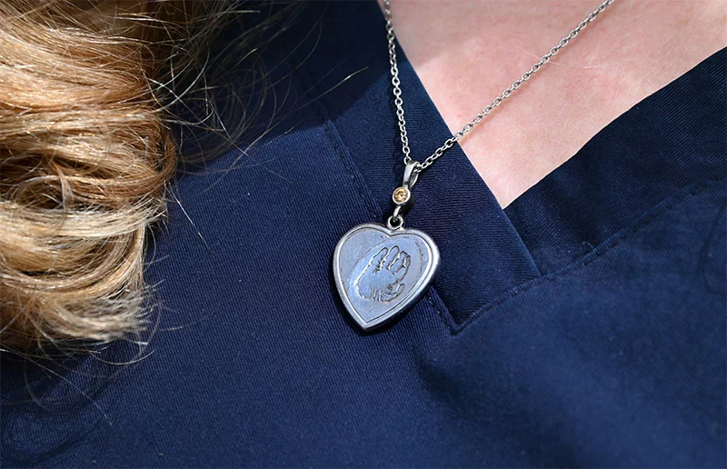 Photo with a close-up of a necklace Vicki McCartney wears with a heart pendant that includes a handprint on it. Vicki McCartney wears a heart pendant necklace with an impression from Palmer's hand. Photo by Sonya Doctorian, UCHealth.