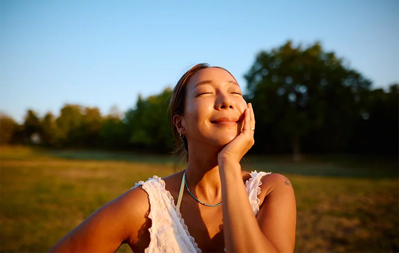 woman in the sunshine, eyes closed and smiling. Pause and take in the good. Positive emotions like awe, gratitude and hope can help cultivate a durability mindset and support your well-being. Photo: Getty Images.